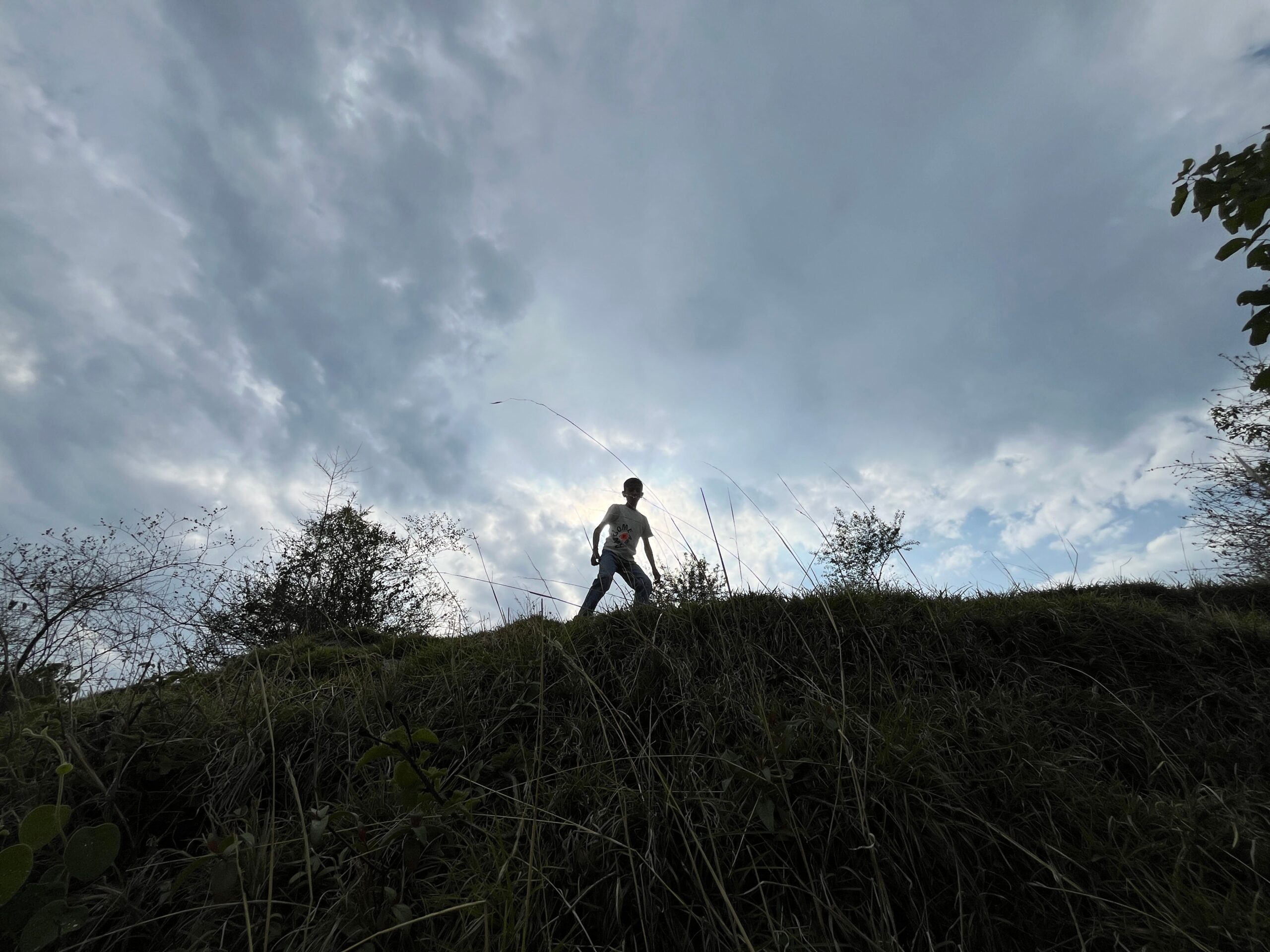 A lone silhouette walking on a grassy hill against a dramatic cloudy sky, creating a serene outdoor scene.