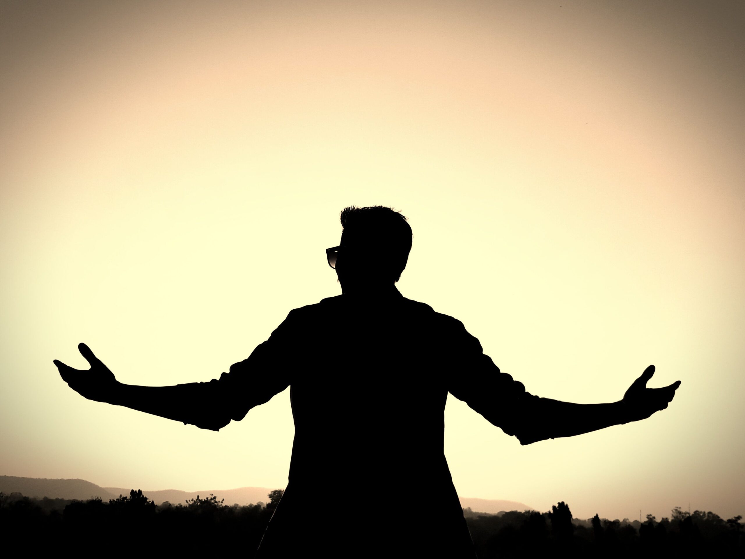 Silhouette of a man with open arms against a vibrant sunset background, symbolizing freedom and peace.
